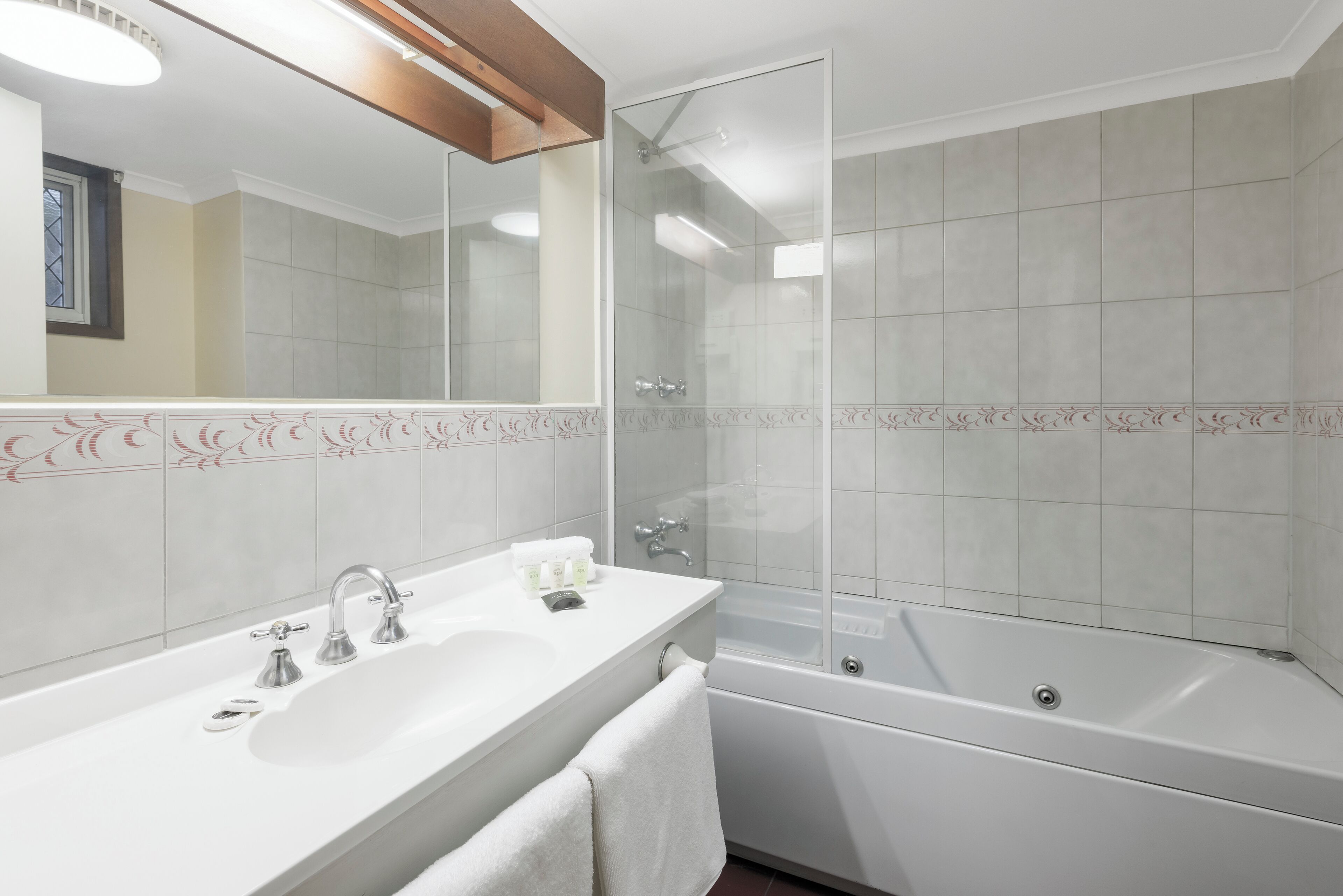 Un baño moderno con un espejo grande, un lavamanos blanco con dos grifos, una ducha con mampara de cristal y una bañera.