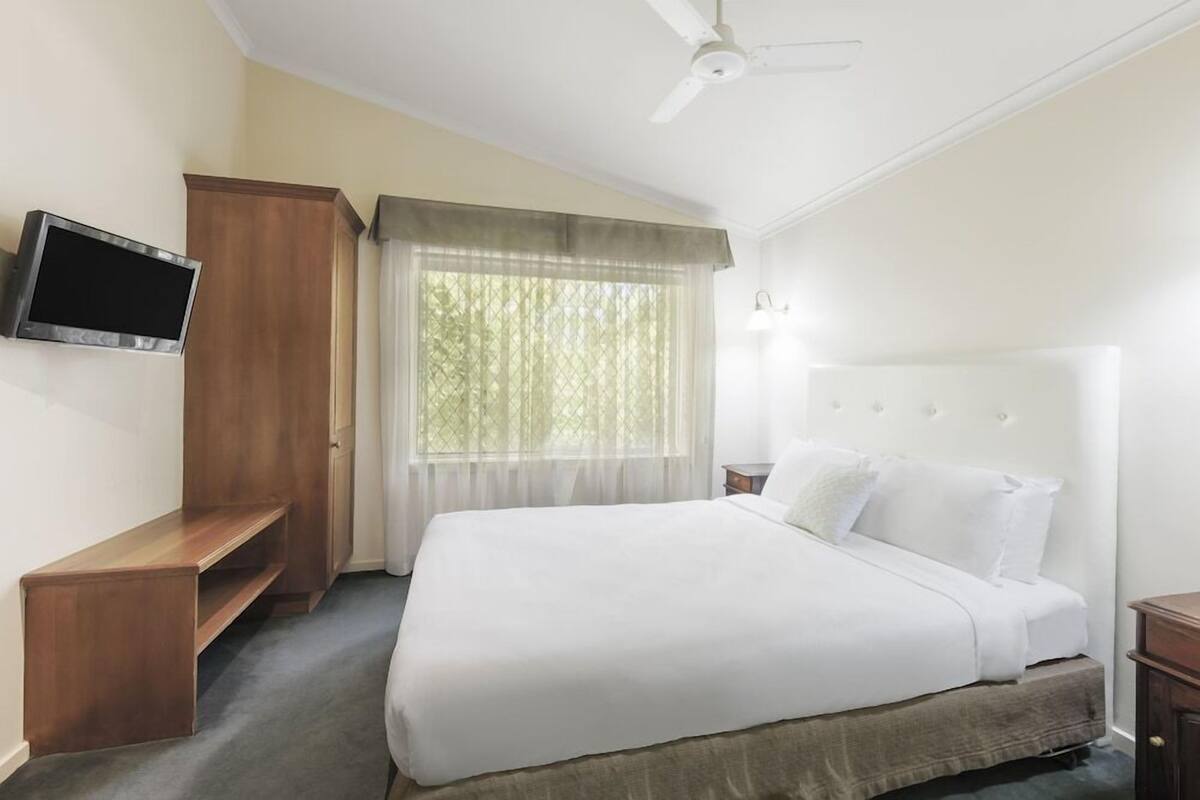 A hotel room with a bed, a television, a wardrobe, and a window with curtains.