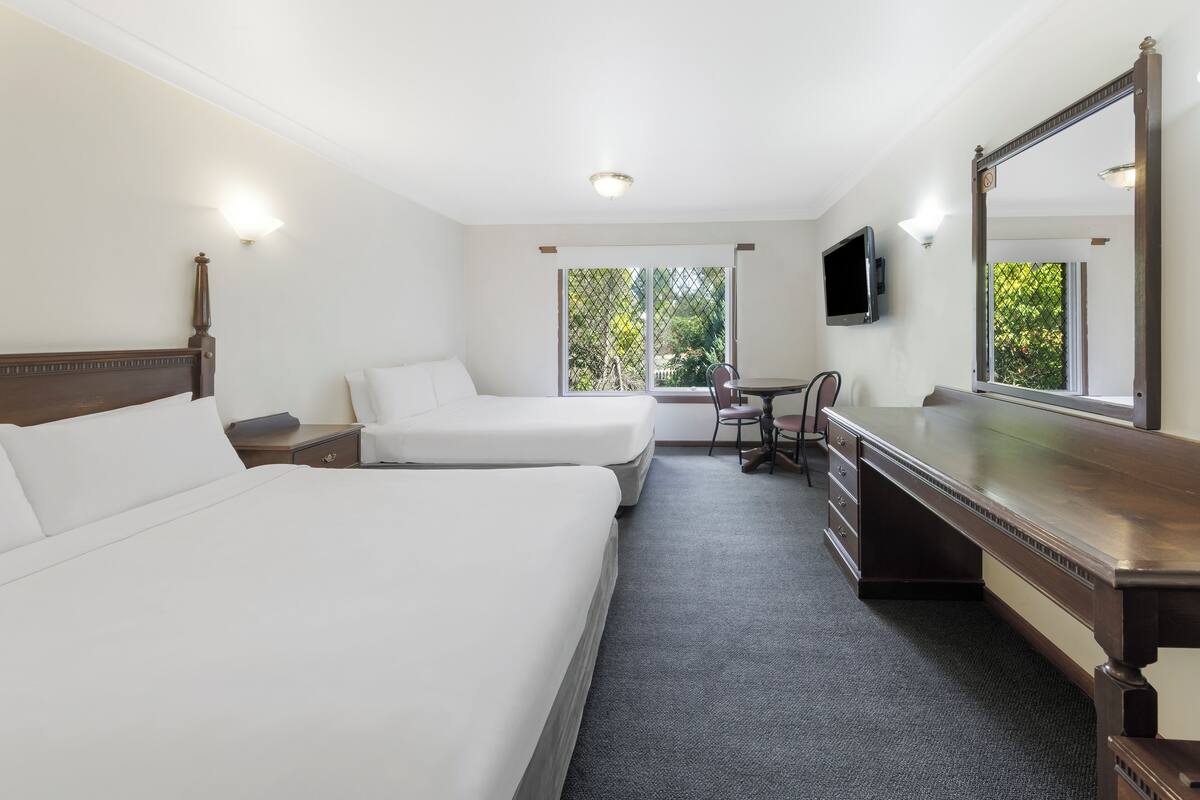 A hotel room with two beds, a desk, a chair, a TV, and a large mirror.