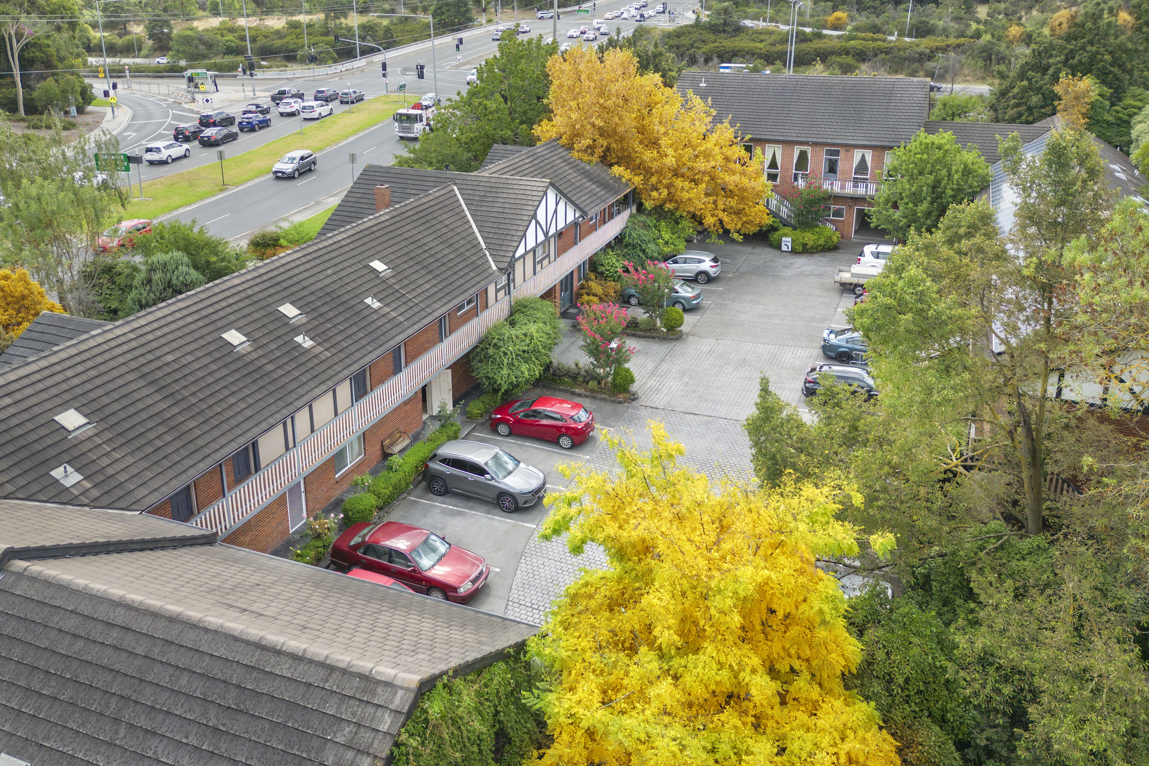Een meerlaags gebouw met een parkeerplaats, omringd door bomen en geparkeerde auto's.