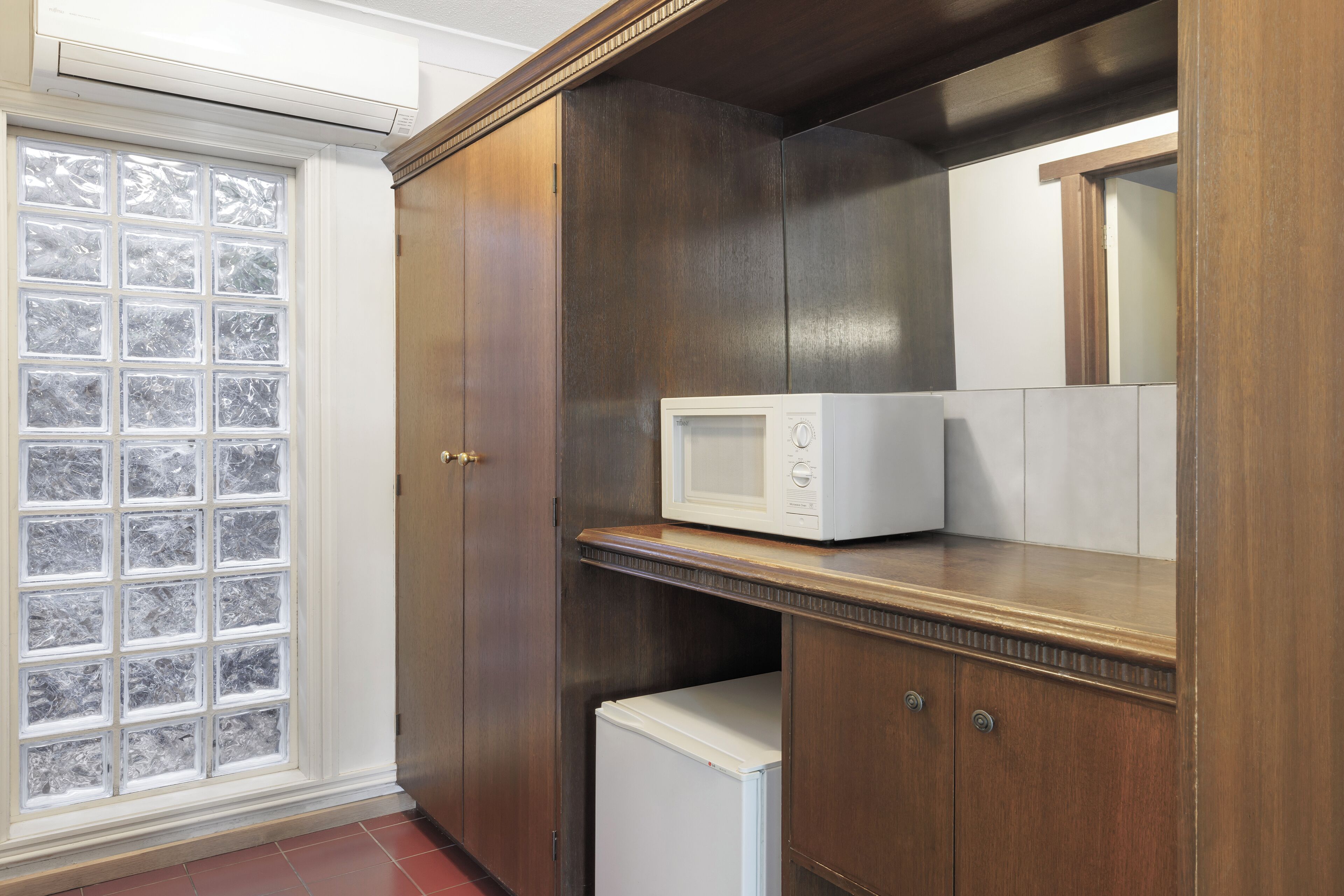 Une cuisine avec un four à micro-ondes posé sur un plan de travail en bois, un réfrigérateur en dessous et une fenêtre à vitre dépolie.