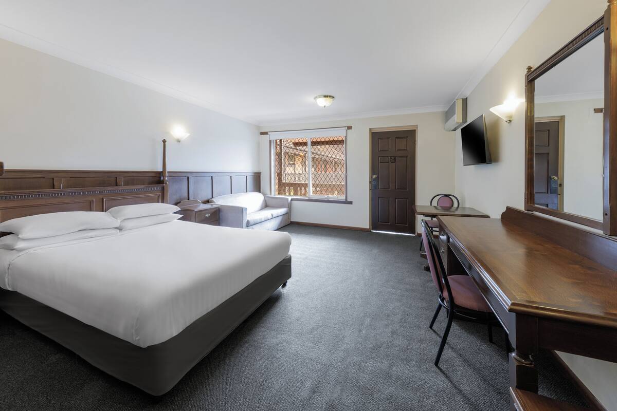 A hotel room with a bed, desk, chair, and a television on the wall.