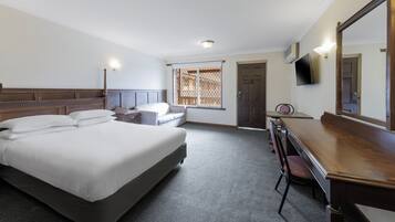 Une chambre d’hôtel avec un lit, un bureau, une chaise et un téléviseur fixé au mur.