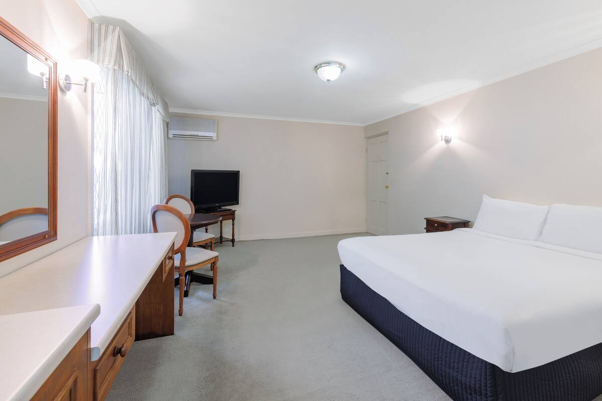 A hotel room with a bed, a desk, a chair, a television, and a mirror.