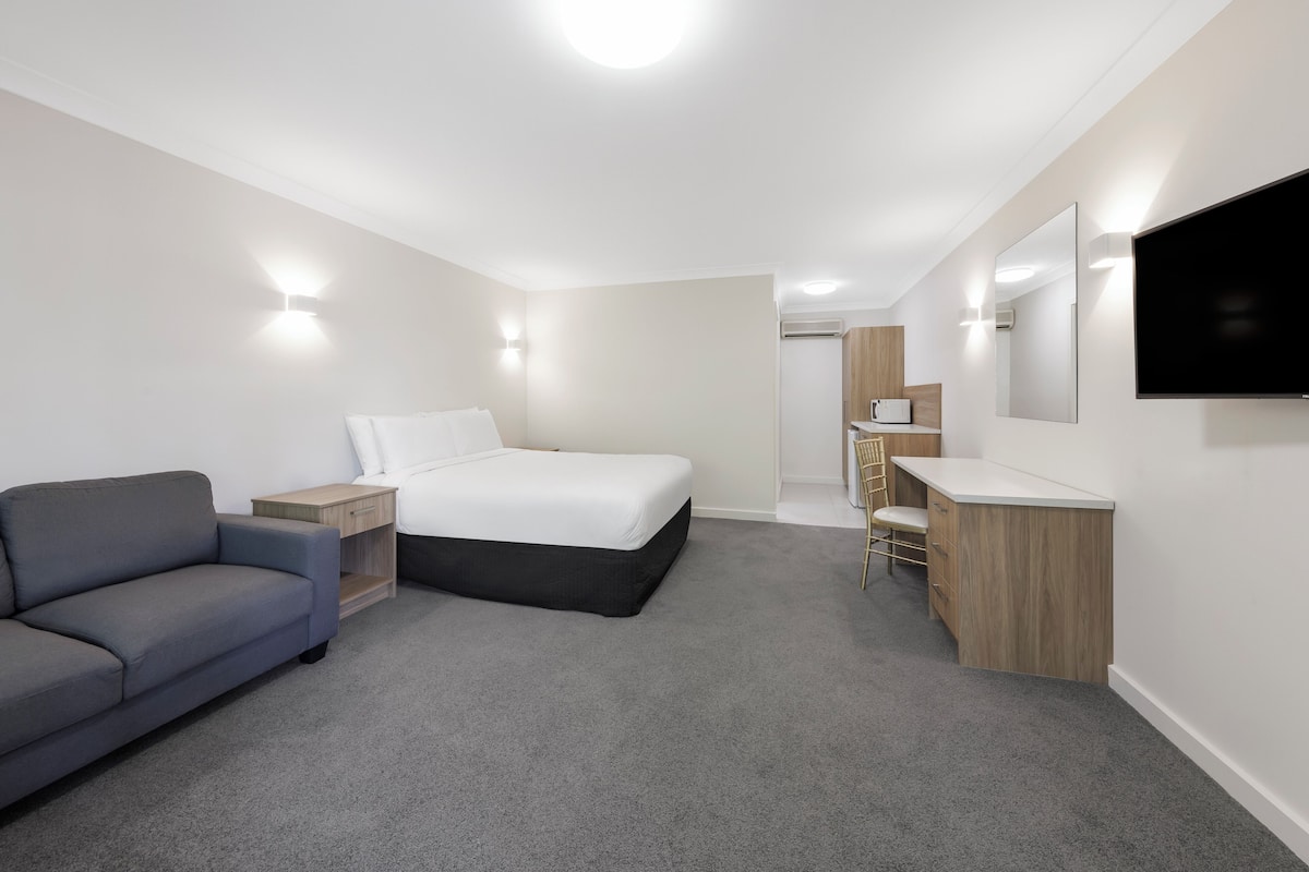 A modern hotel room with a bed, a sofa, a desk, and a TV.