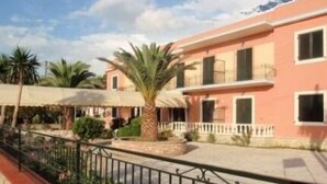 A pink building with balconies, surrounded by palm trees and a fence. - Argo Hotel (Corfu)