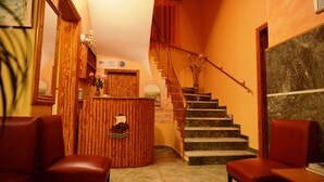 A reception area with a wooden desk, a staircase, and two red chairs. - Argo Hotel (Corfu)