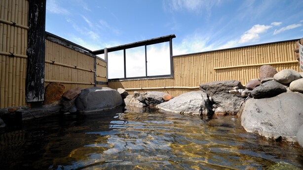 A traditional Japanese onsen with a wooden bathhouse, a small stream, and rocks. - Hotel Pony Onsen (Towada)