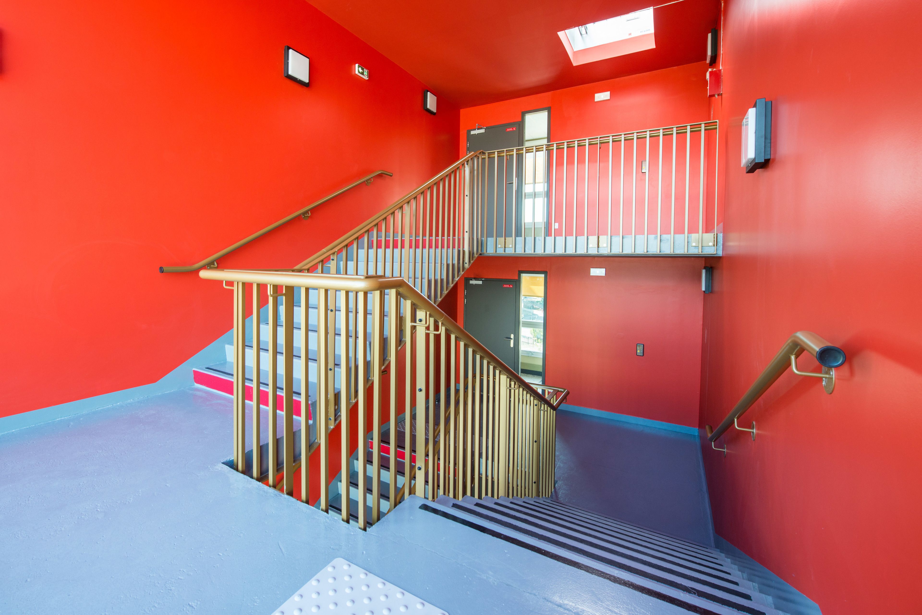 Una escalera con barandillas metálicas y piso azul, que conduce a un segundo nivel.