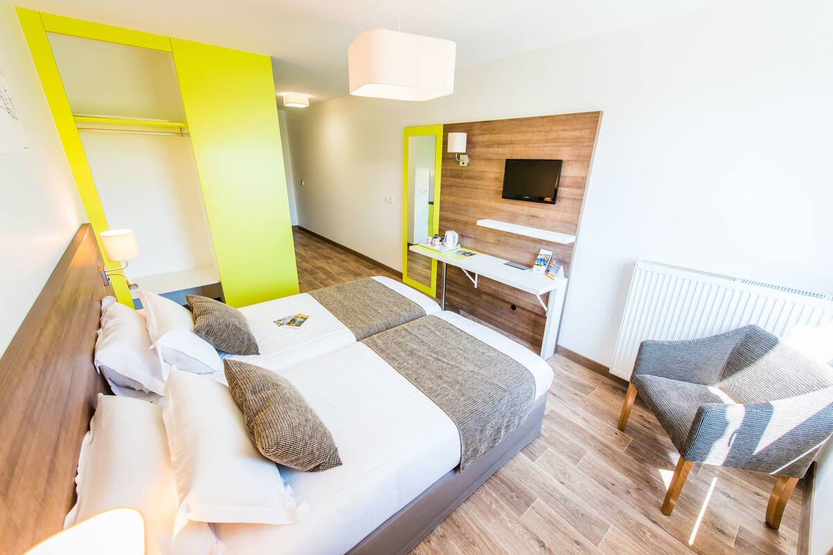A modern hotel room with a bed, a desk, a chair, and a TV.