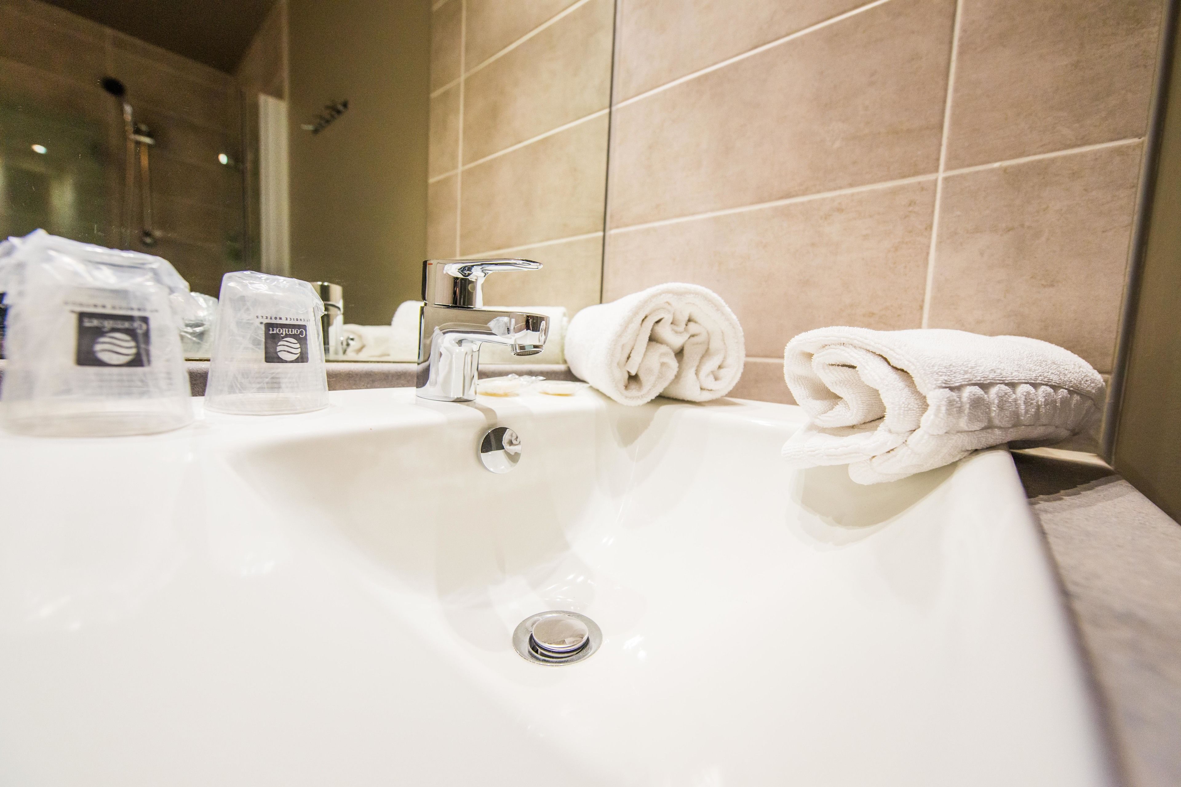 A white bathroom sink with a chrome faucet, two bottles of toiletries, and a rolled white towel on the edge.