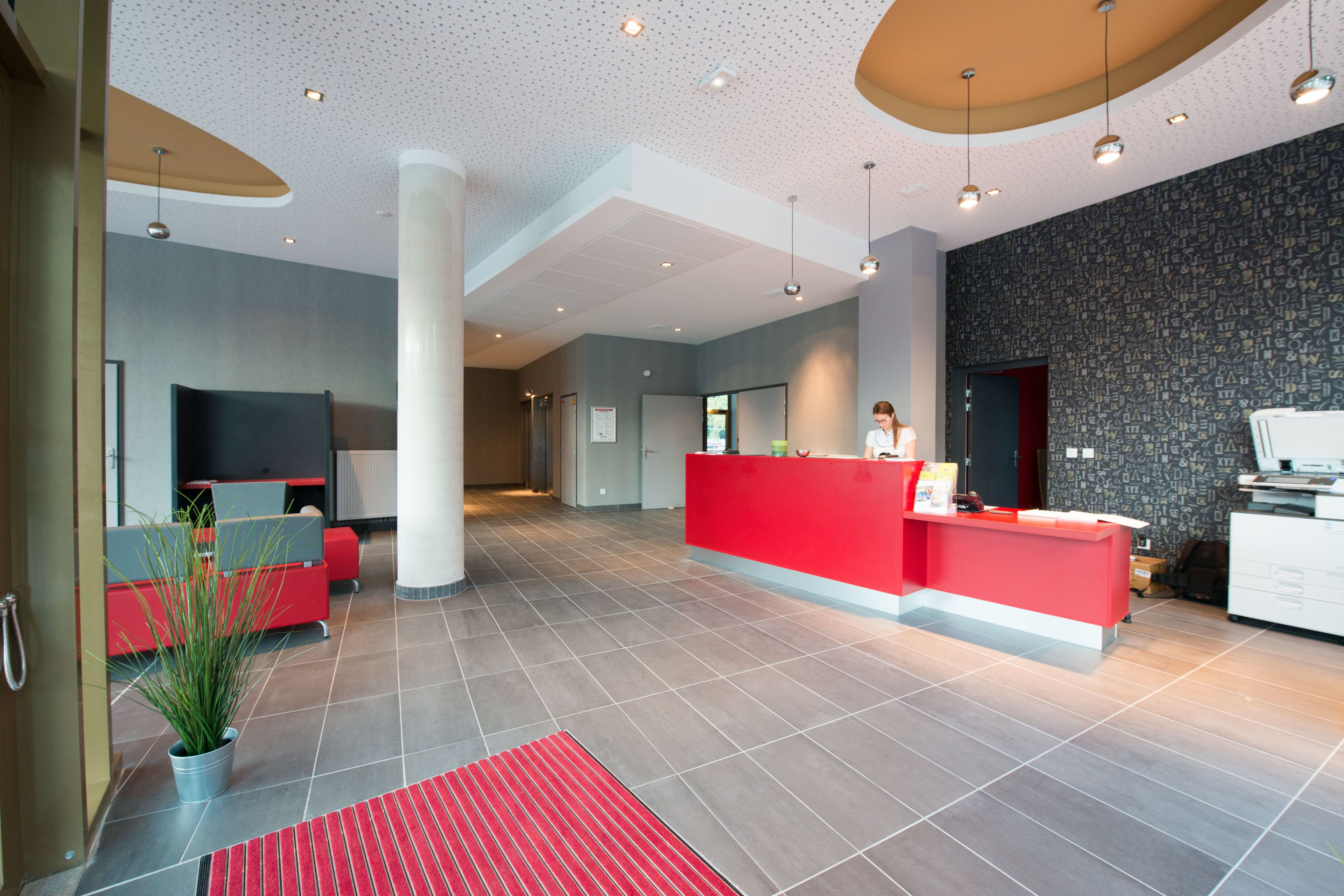 A modern hotel lobby with a reception desk, seating area, and a large potted plant.