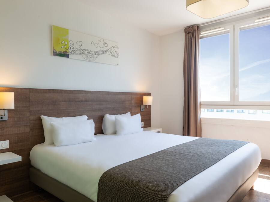 A hotel room with a large bed, two bedside lamps, a wall-mounted artwork, and a window with curtains.