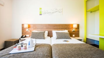 A hotel room with two beds, a bedside table with a lamp, a wall-mounted artwork, and a bright yellow accent wall.