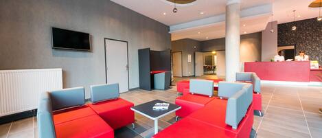 A modern lobby with red and grey seating, a flat-screen TV, and a reception desk.