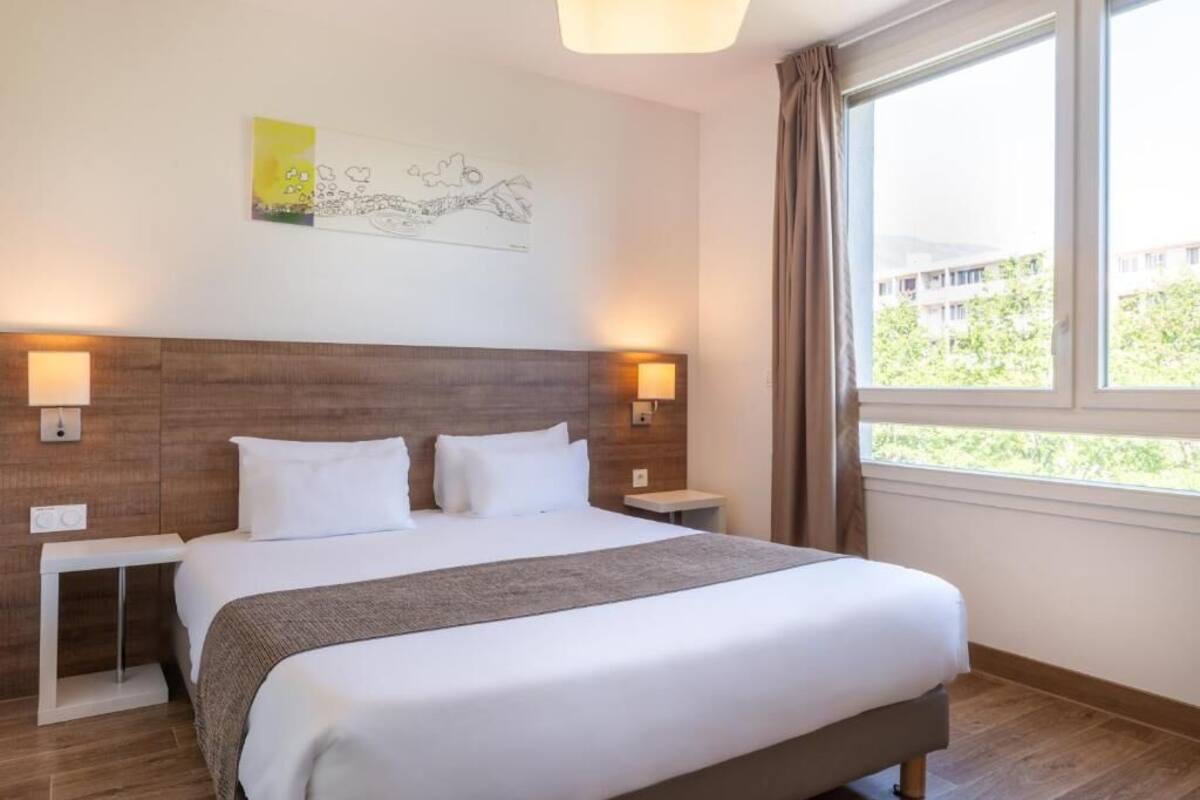 A hotel room with a large bed, two bedside tables, a headboard, and a window with curtains.