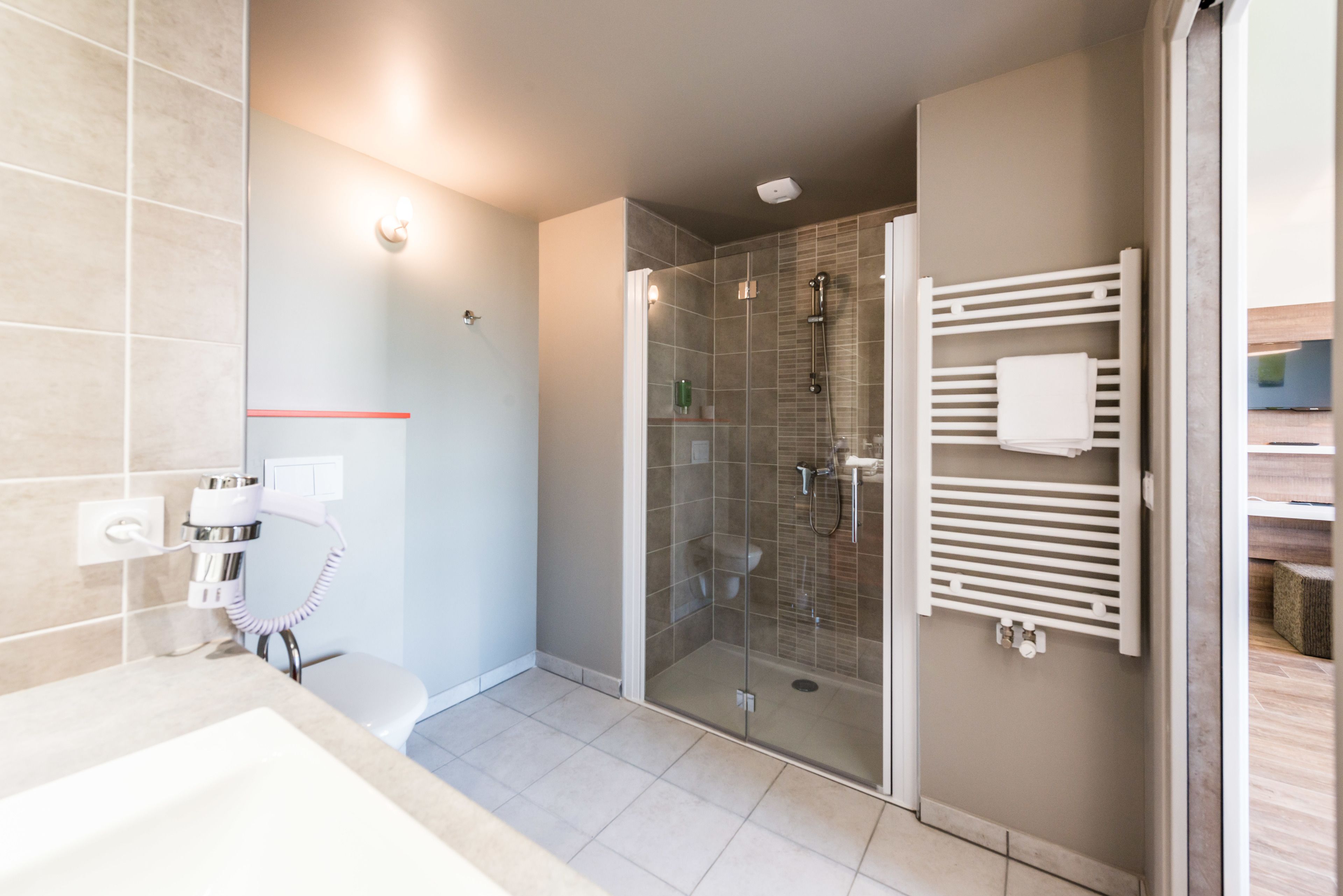 A modern bathroom with a glass-enclosed shower, a white sink, and a towel rack.