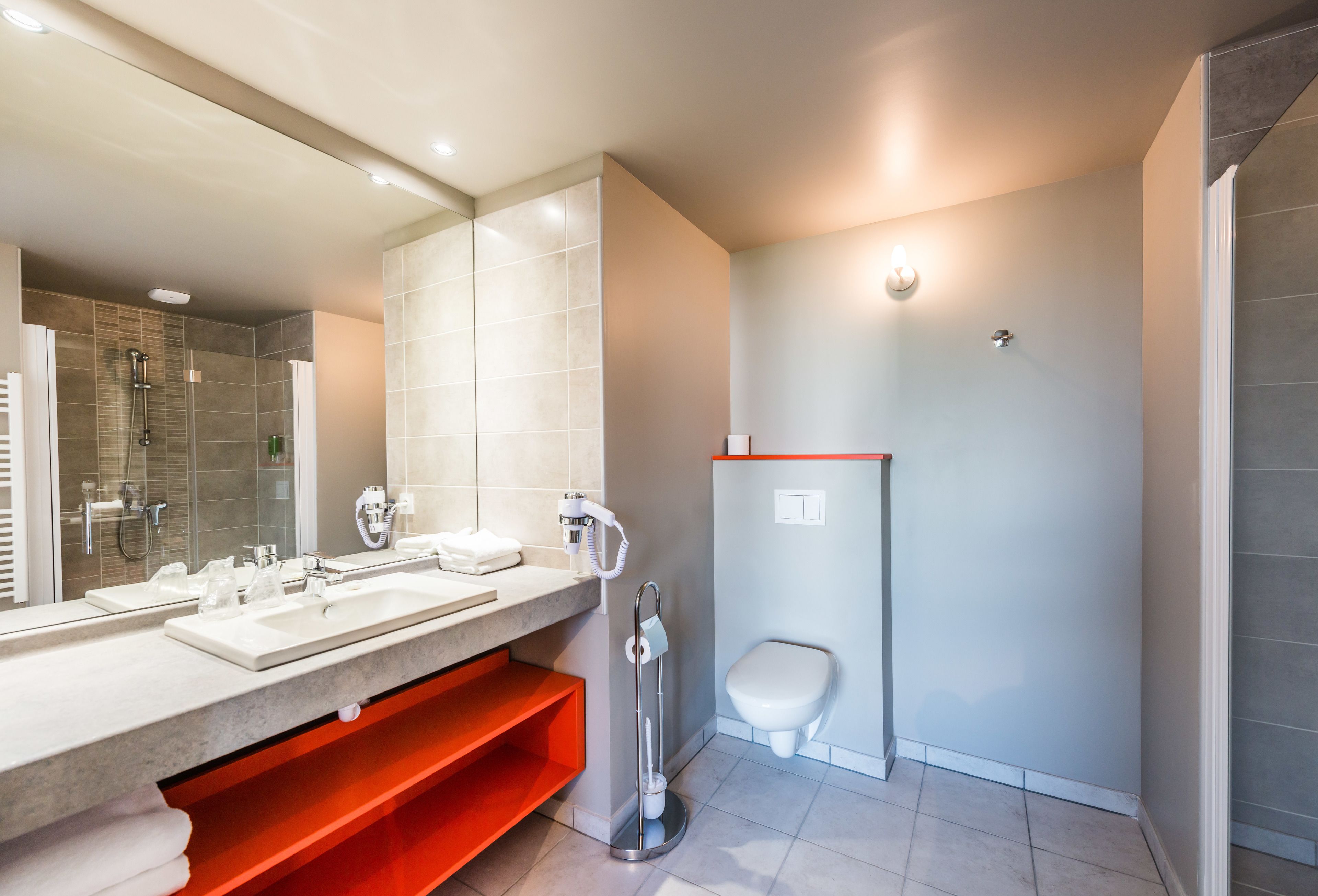 A modern bathroom with a large mirror, two sinks, a shower, and a toilet.