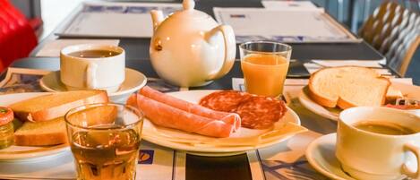 Un desayuno con tetera, tazas, tostadas, salchichas y jugo sobre una mesa.