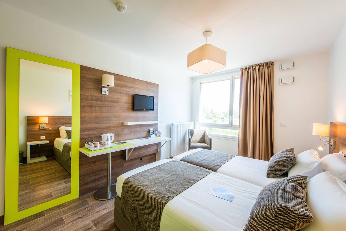 A hotel room with a bed, a desk, a chair, a TV, and a window with curtains.