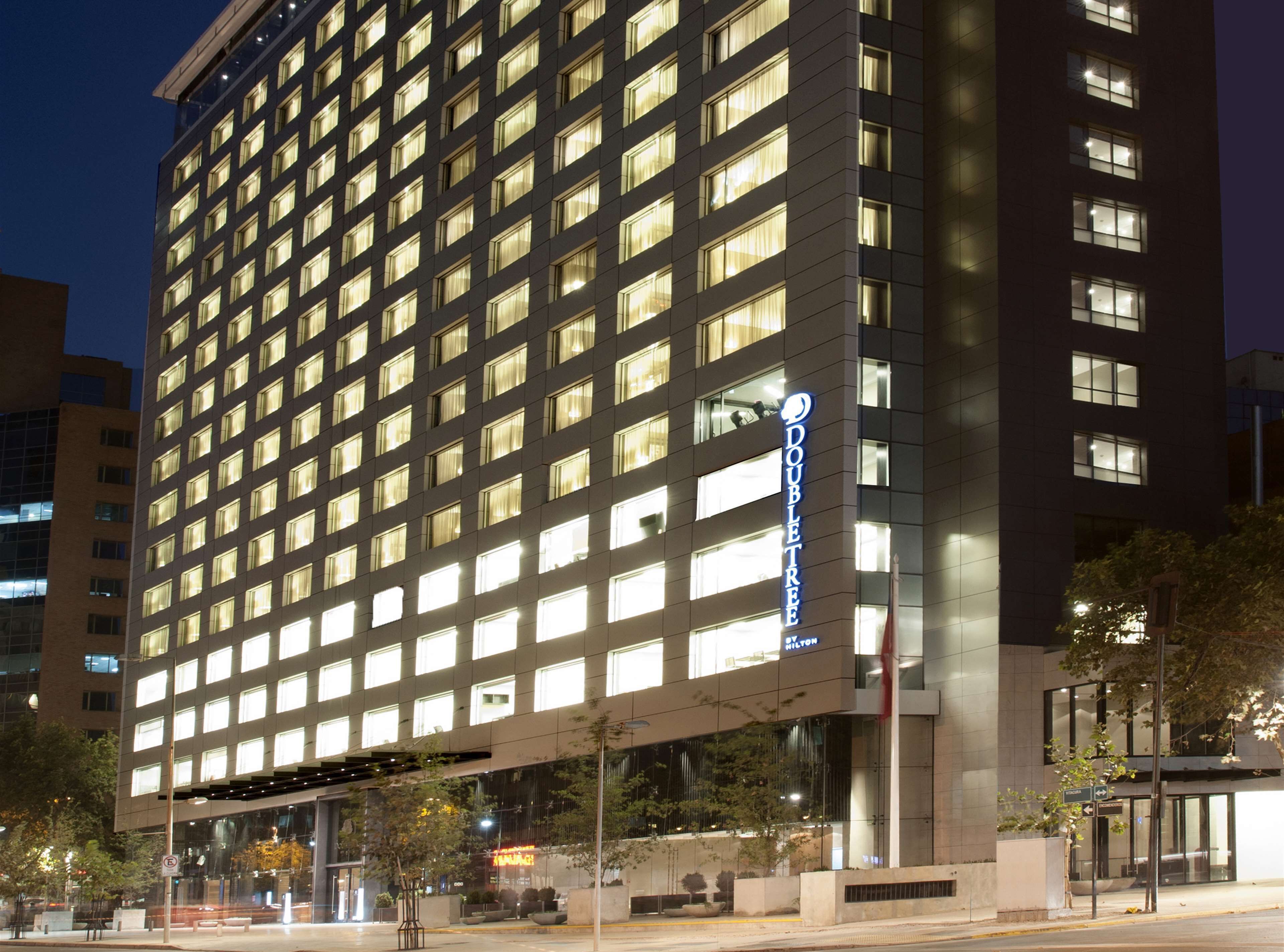 Un hôtel de grande hauteur, avec une façade constituée d’une grille de fenêtres illuminées, une enseigne « DOUBLETREE » bien visible et une architecture moderne.