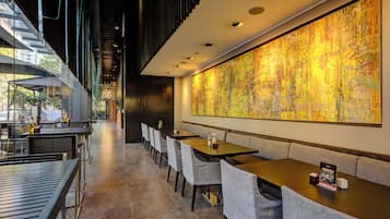 Um restaurante moderno com um balcão extenso, várias mesas e um grande quadro abstrato na parede.