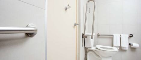 Un baño moderno con inodoro, barra de apoyo y zona de ducha.