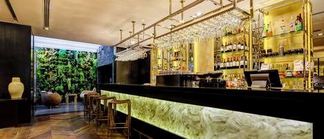 Zona de bar con mostrador de mármol, taburetes y una variedad de botellas y vasos.