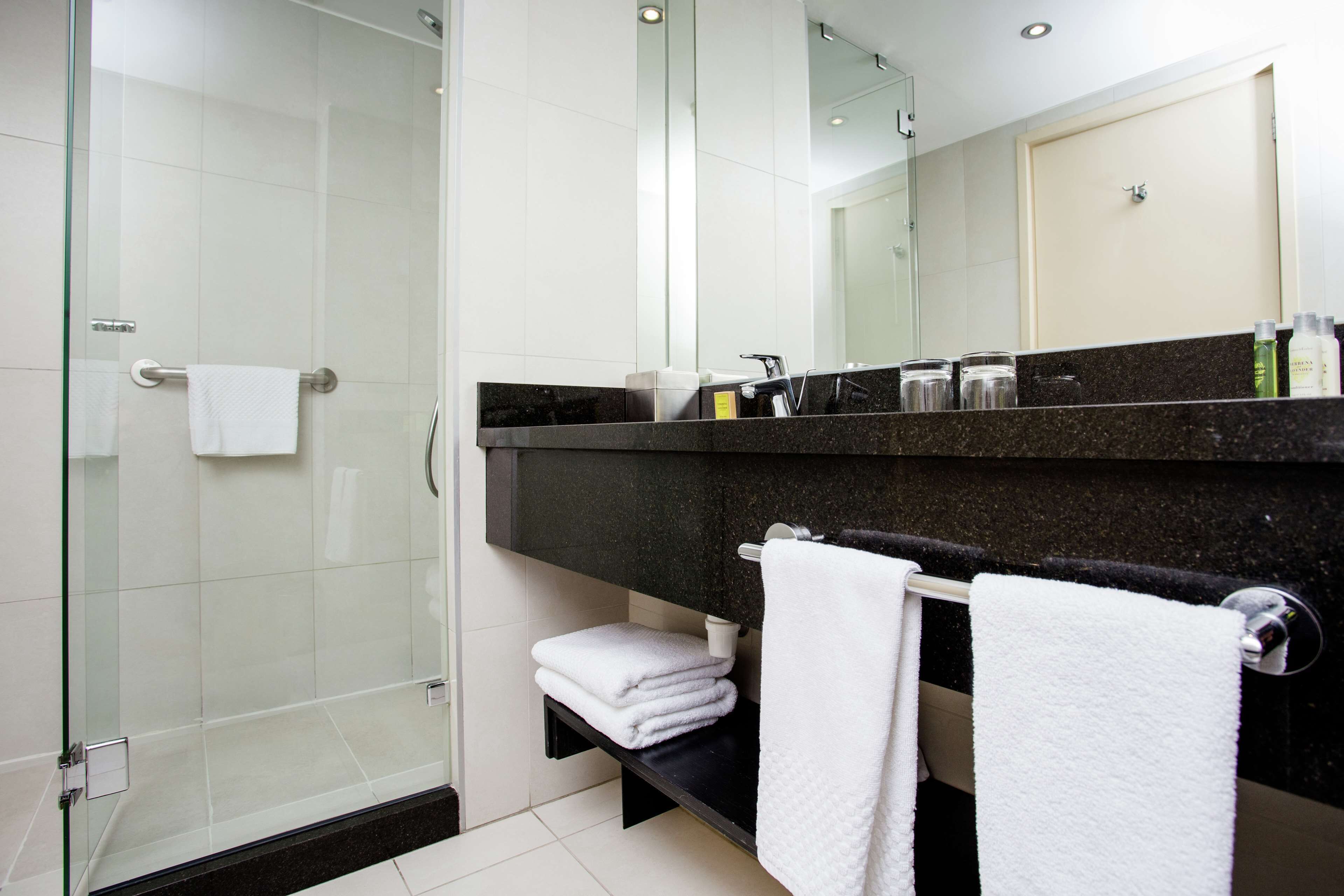 Une salle de bain moderne avec une douche à l’italienne en verre, un plan de toilette noir et des serviettes blanches.