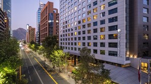 Een modern hotel met een rooster van ramen, een straat met bomen en een berg op de achtergrond.