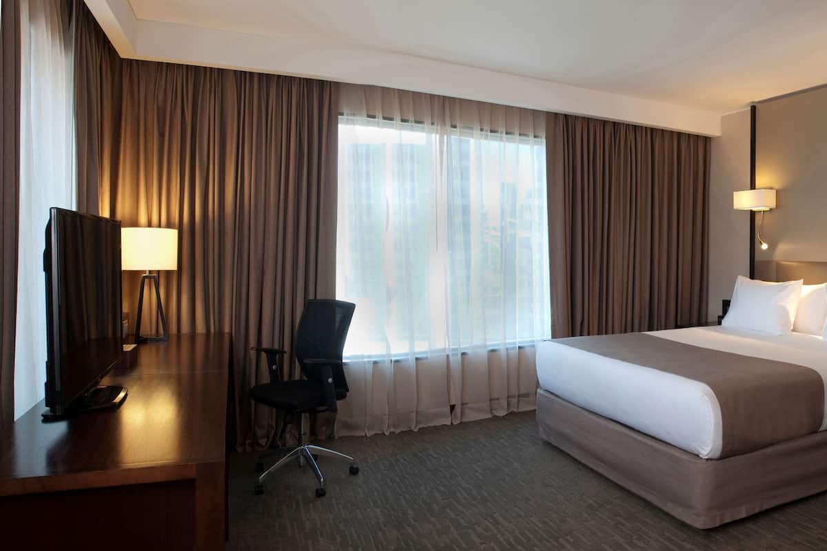 Ein Hotelzimmer mit einem großen Bett, einem Schreibtisch mit Stuhl, einem Fernseher und zwei Nachttischlampen.