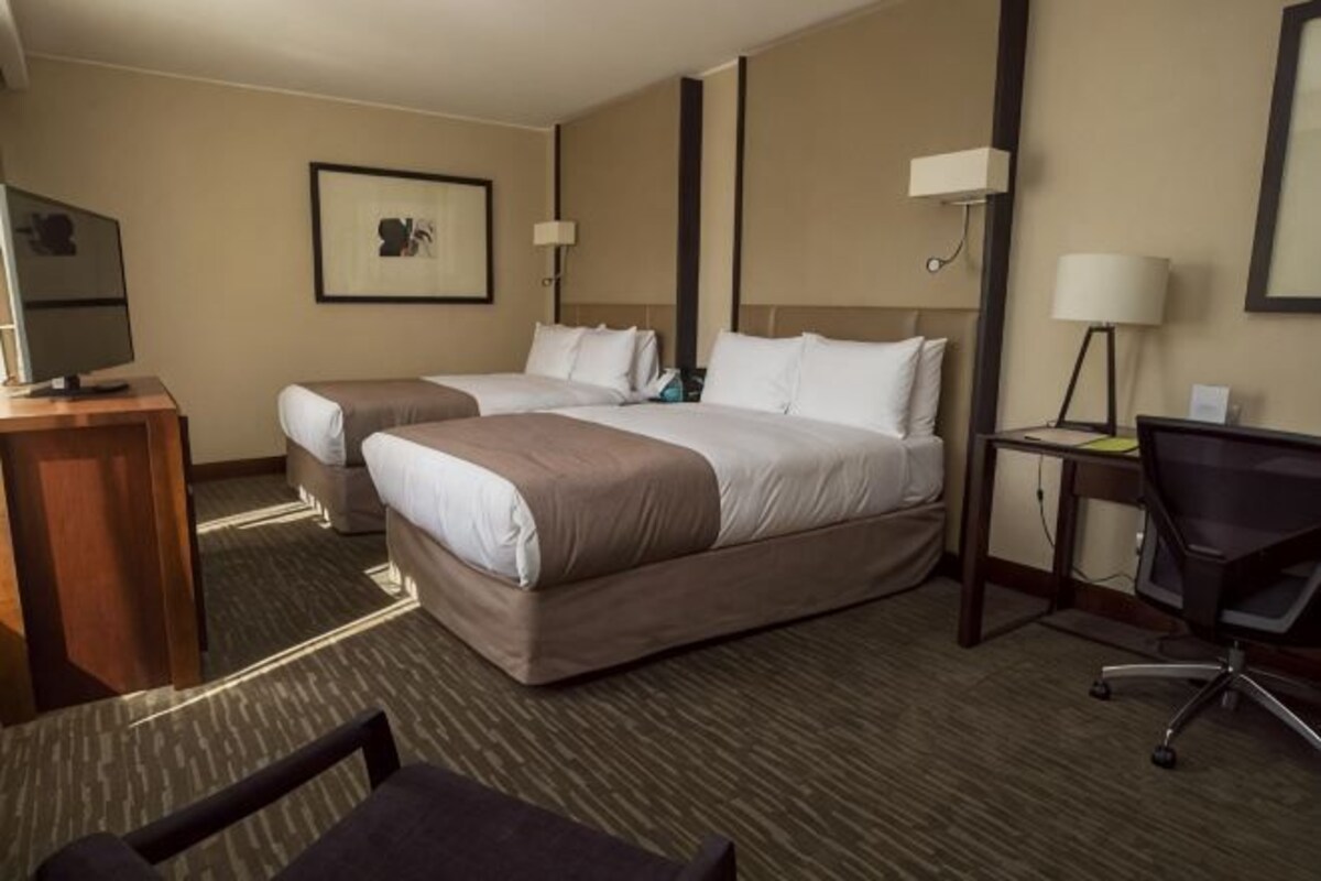 Habitación de hotel con dos camas, un escritorio, una silla y un televisor.