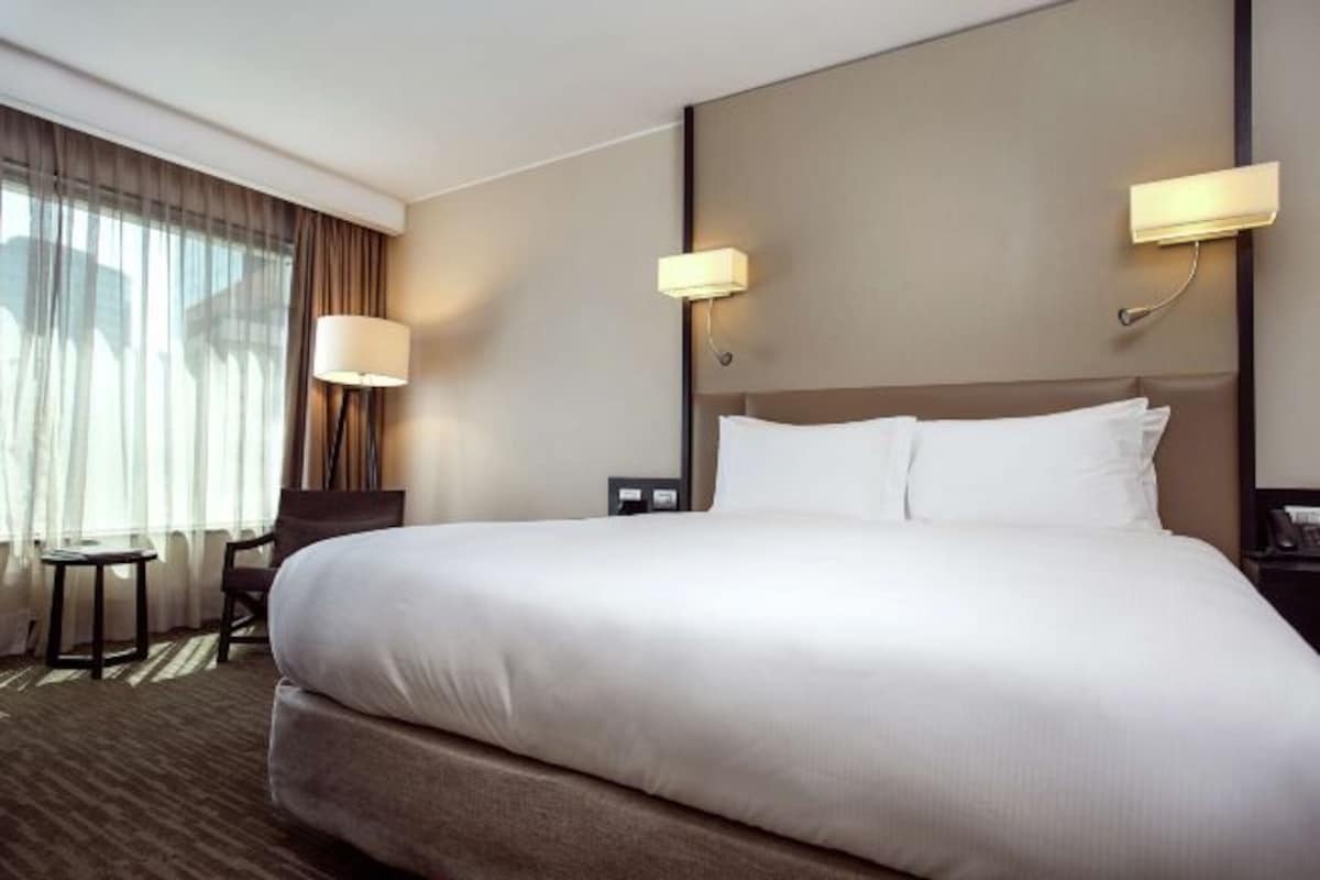Une chambre d’hôtel avec un grand lit, deux lampes de chevet, une petite table et une chaise.