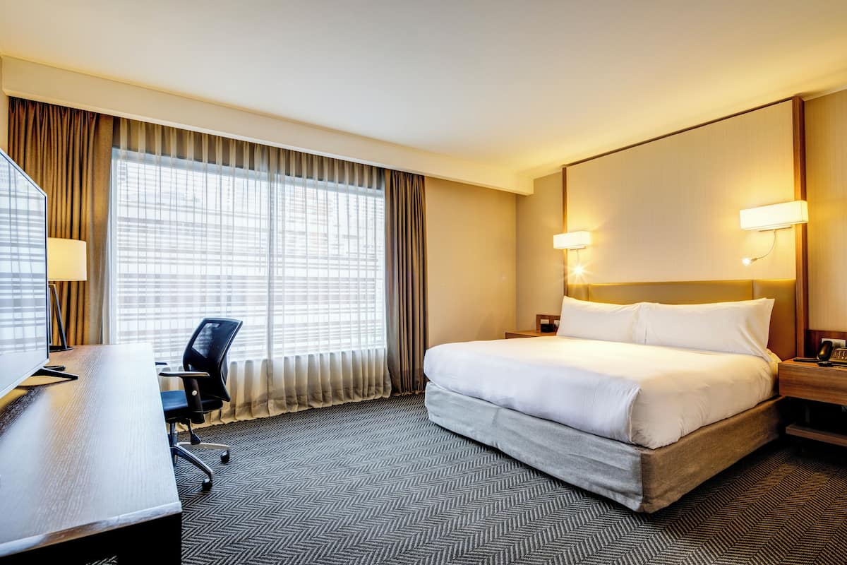 Ein Hotelzimmer mit einem großen Bett, einem Schreibtisch mit Stuhl, einem Fenster mit Vorhängen und zwei Nachttischlampen.