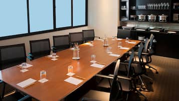 Ein Konferenzraum mit einem langen Tisch, Stühlen, einer Projektionsleinwand und einem Büfettbereich mit Gläsern.