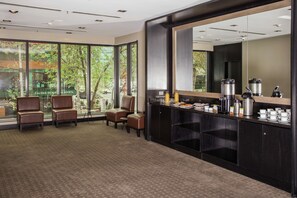 Een moderne hotellobby met een groot raam, lederen zitplaatsen, een koffiehoek en een grote spiegel.