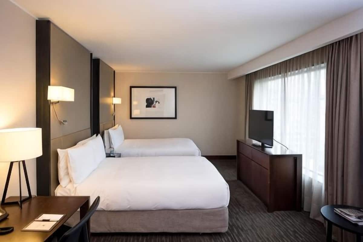 Une chambre d’hôtel avec deux lits, un bureau, une chaise, une télévision et un tableau encadré au mur.
