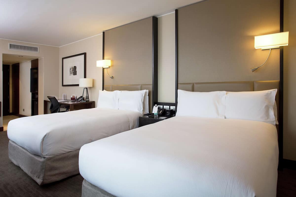 Ein Hotelzimmer mit zwei Betten, einem Schreibtisch, einem Stuhl und einem gerahmten Bild an der Wand.