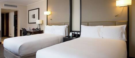 A hotel room with two beds, a desk, a chair, and a framed picture on the wall.