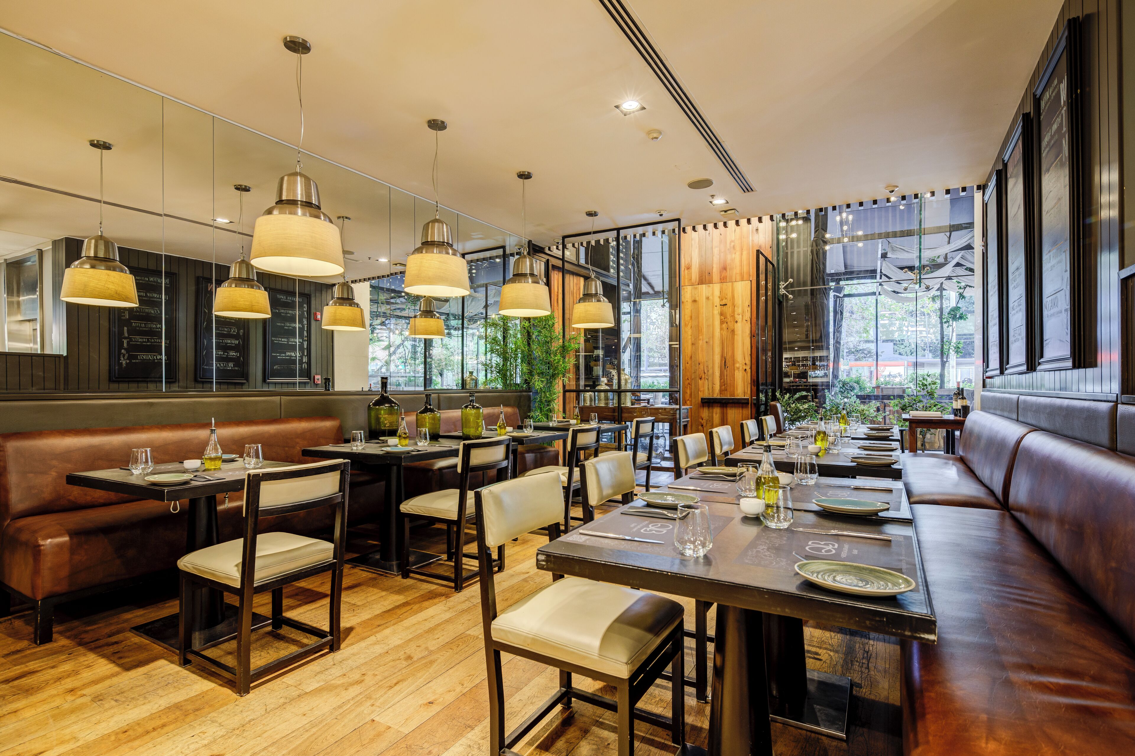 A restaurant with wooden flooring, leather booths, and pendant lighting. Tables are set with plates, glasses, and cutlery.