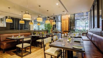 A restaurant with wooden flooring, leather booths, and pendant lighting. Tables are set with plates, glasses, and cutlery.