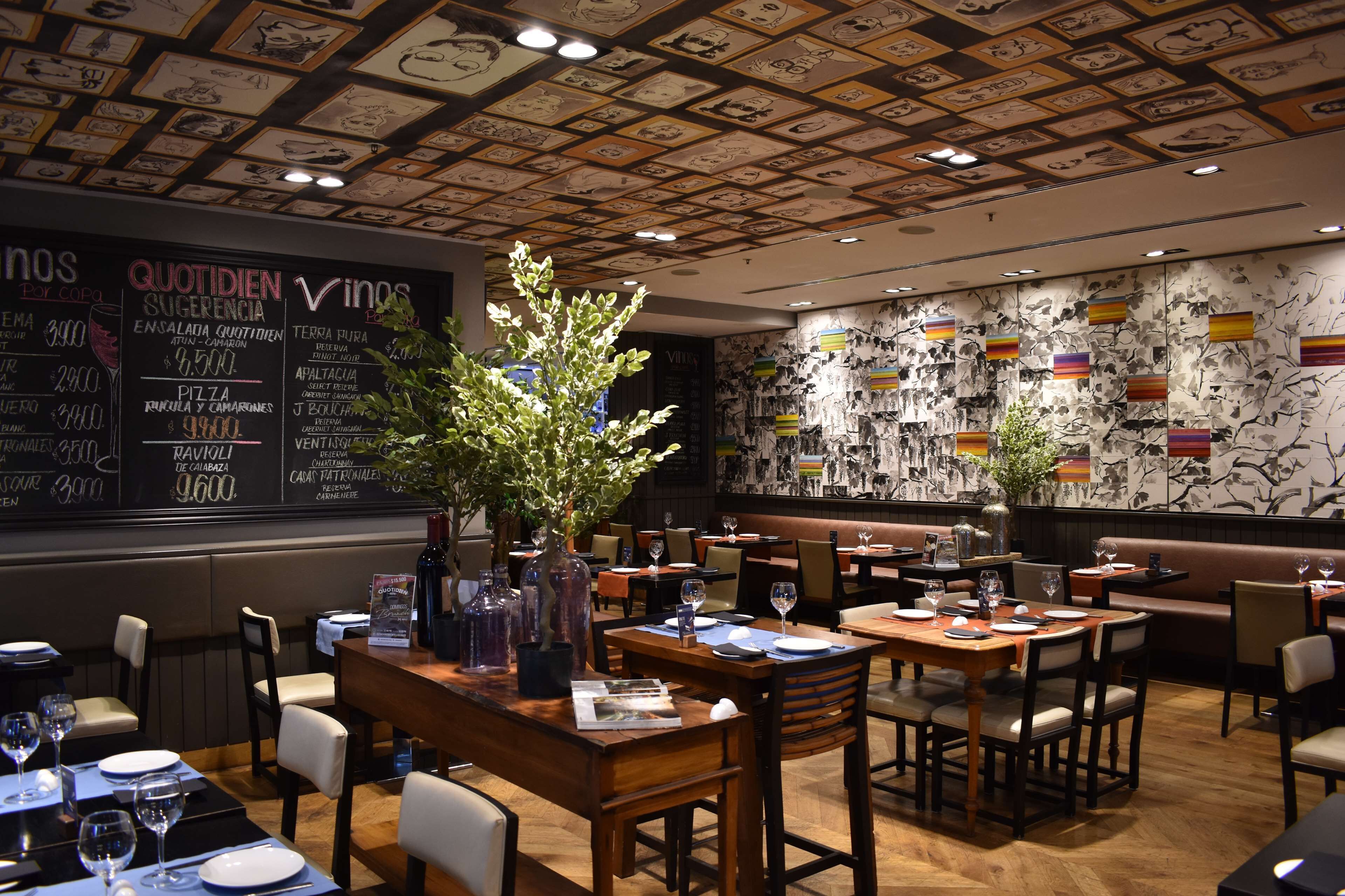 Un interior de restaurante con mesas y sillas de madera, un menú en la pizarra y un techo decorativo.
