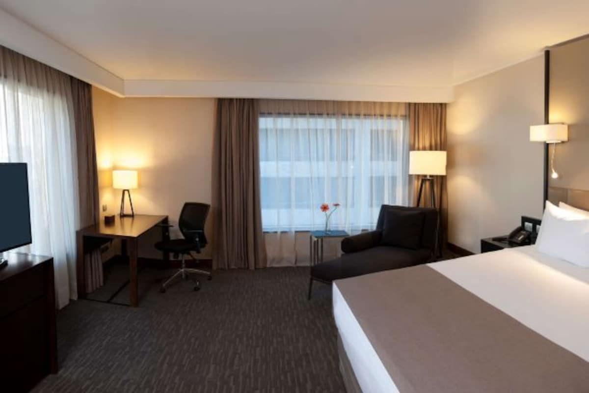Une chambre d’hôtel avec un grand lit, un bureau avec une chaise, une petite table avec une lampe et un téléviseur.