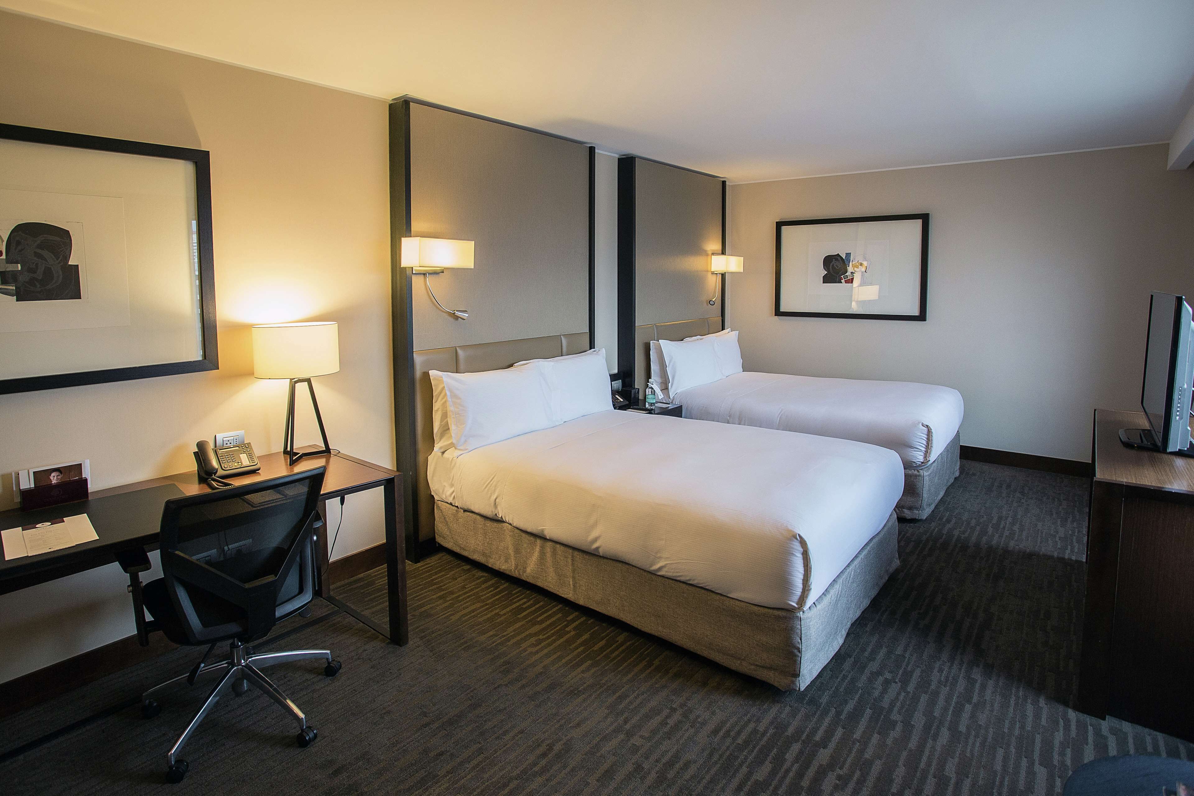 Une chambre d’hôtel avec deux lits, un bureau avec une chaise, un téléphone et une télévision.