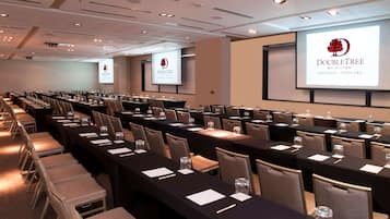 Un salón de conferencias con filas de mesas y sillas, equipado con proyectores y pantallas que muestran el logotipo de DoubleTree.