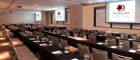 Un salón de conferencias con filas de mesas y sillas, equipado con proyectores y pantallas que muestran el logotipo de DoubleTree.