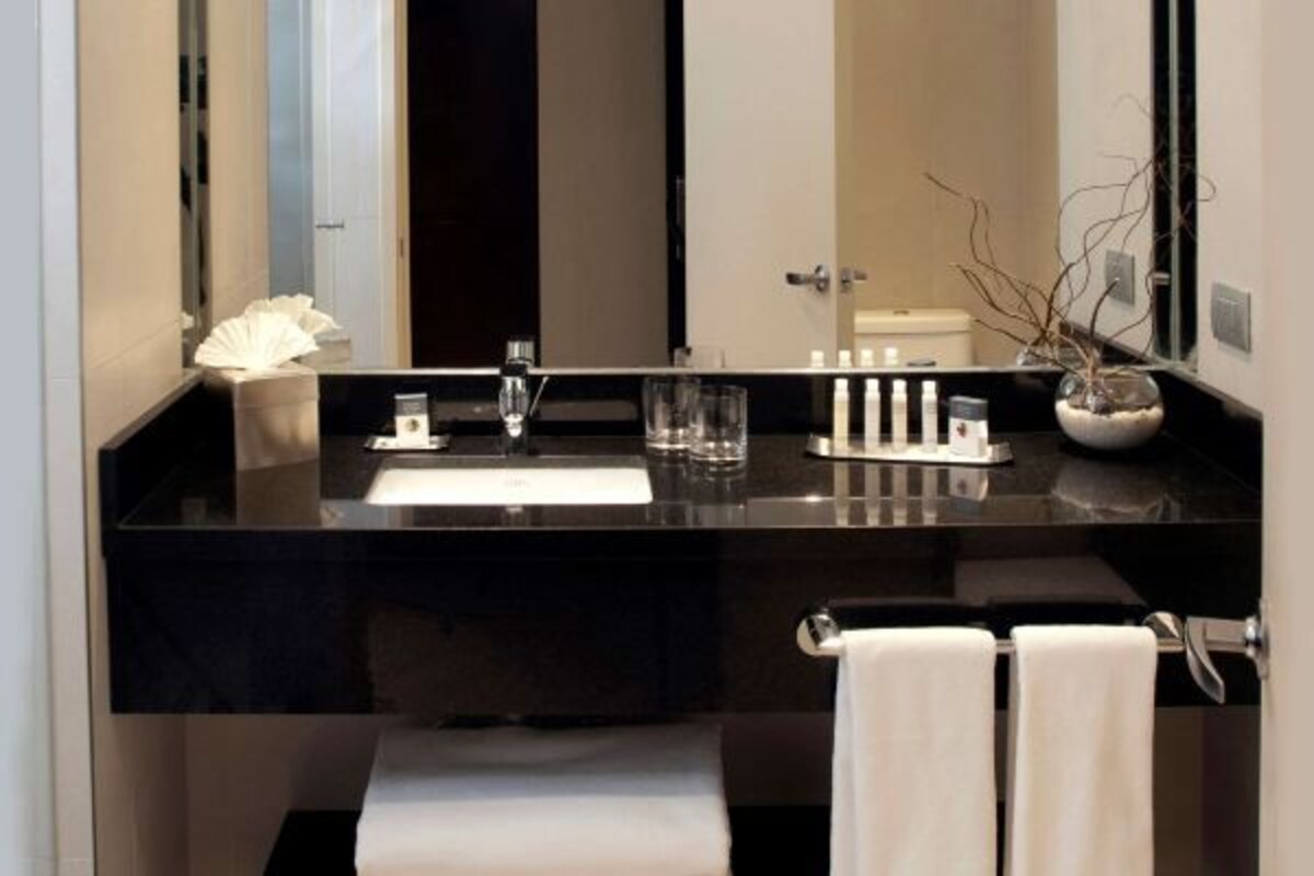 Une salle de bain moderne avec un plan de toilette noir, un miroir, un lavabo et deux serviettes blanches.