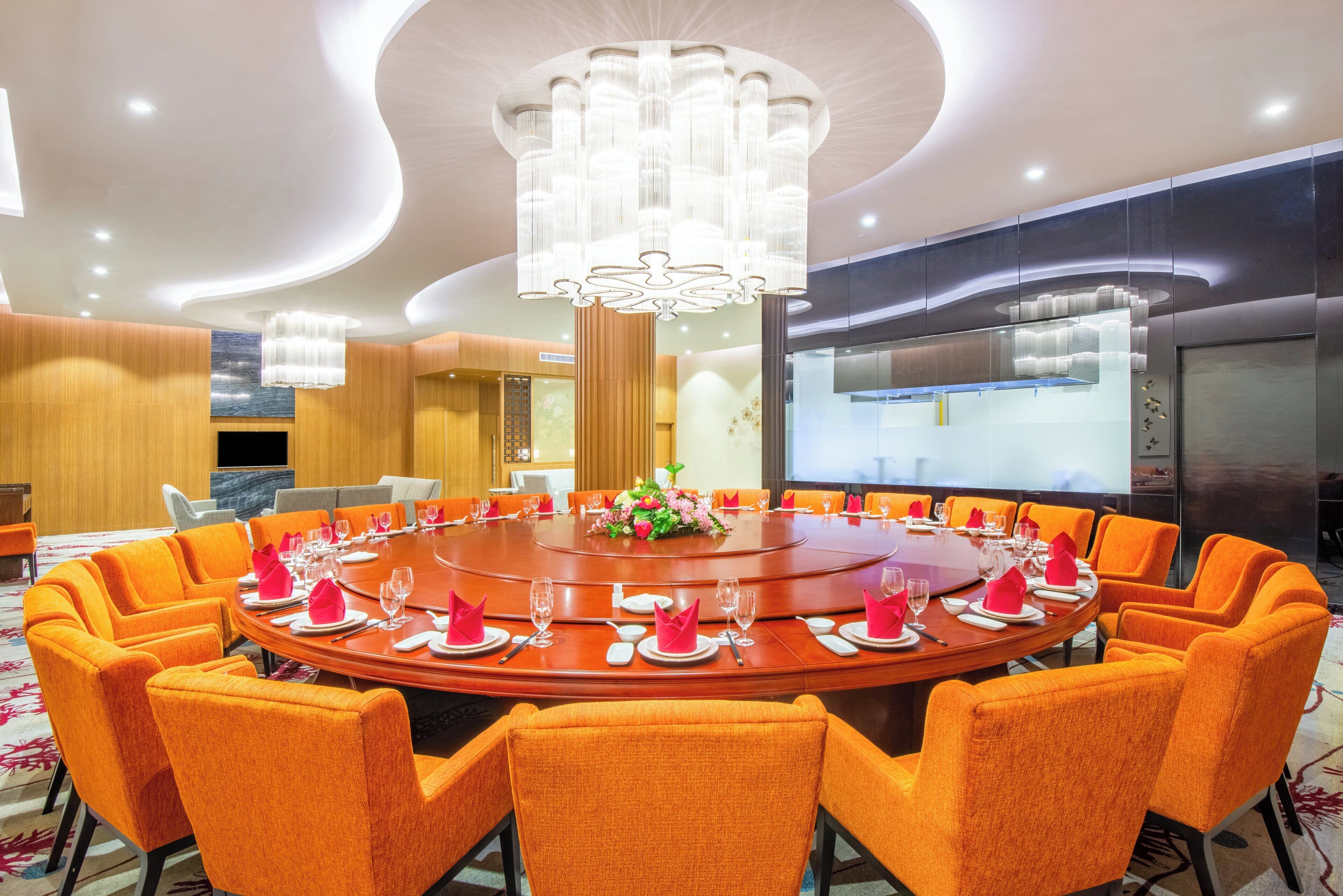 Ein Konferenzraum mit rundem Tisch, orangenen Stühlen und einer Chandelier.
