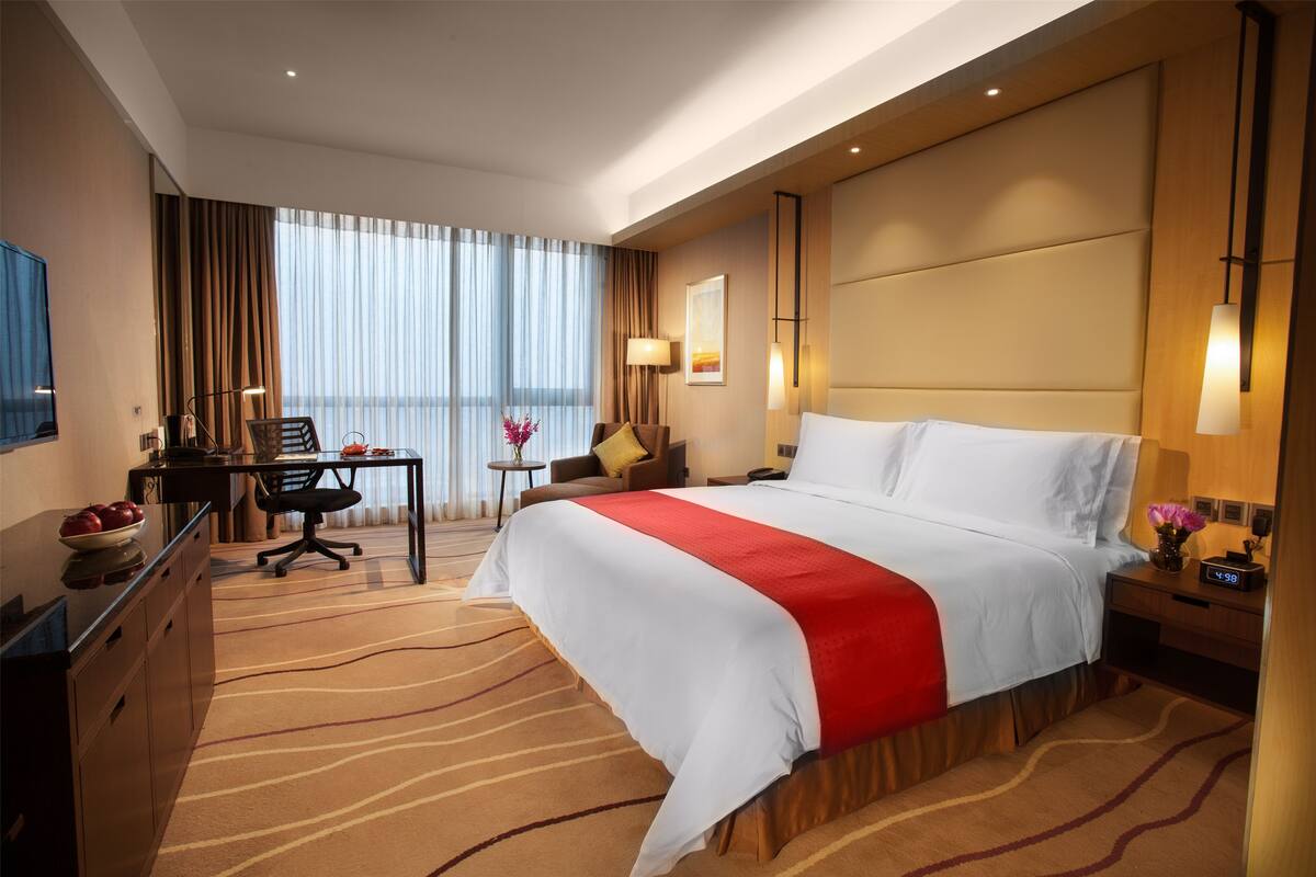 A hotel room with a large bed, a desk with a chair, a TV, and a window with curtains.