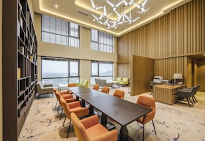 Un salón de conferencias con una larga mesa, sillas color naranja, una estantería y grandes ventanales con vistas panorámicas.
